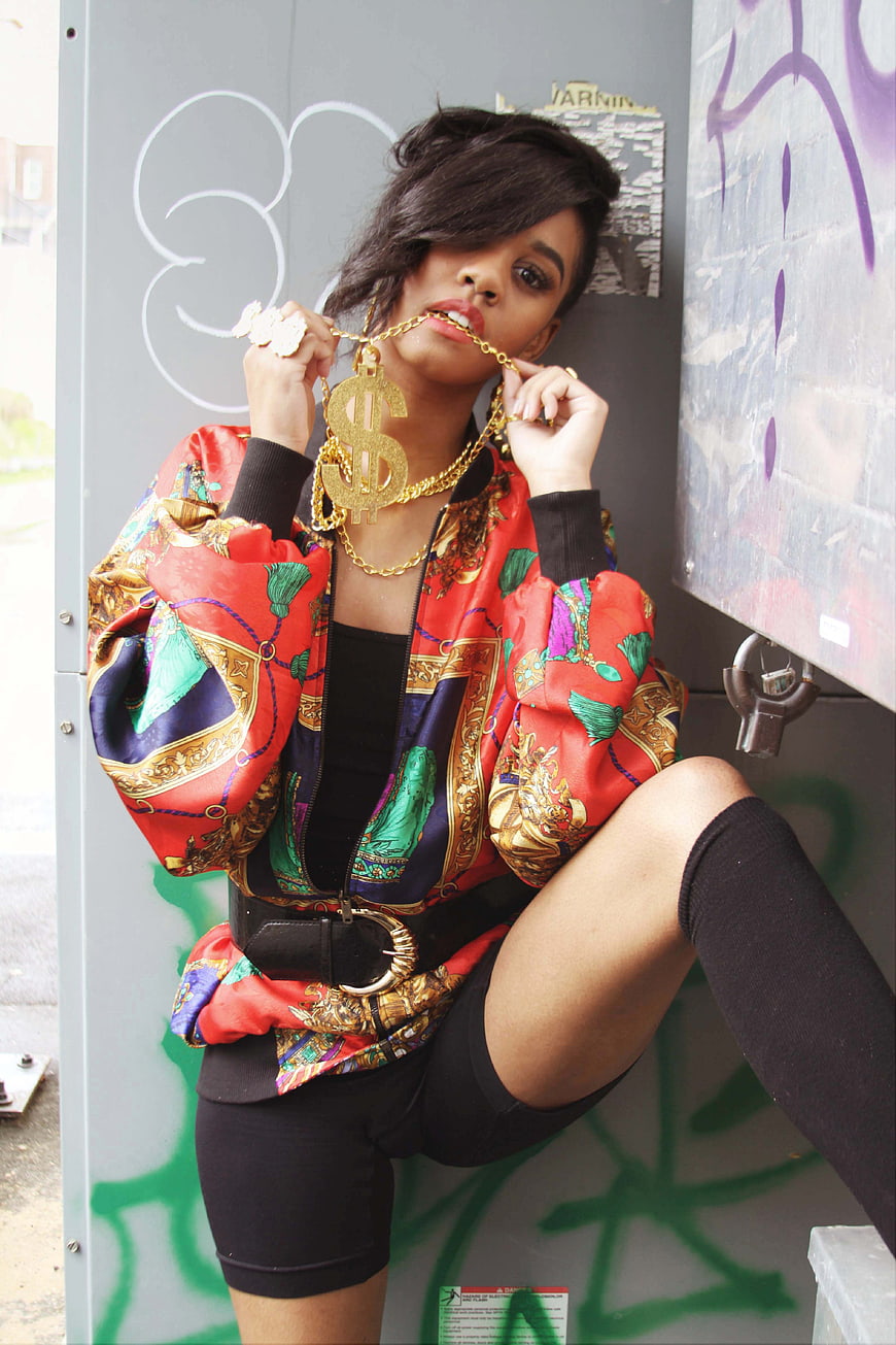 Woman in colorful bomber jacket with gold dollar sign necklace