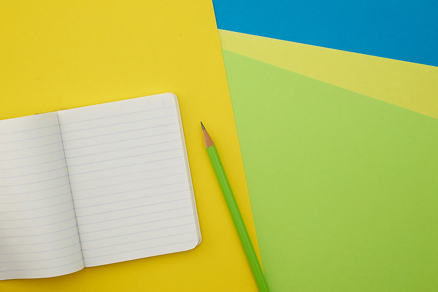 Flat lay of open notebook and green pencil on colorful background