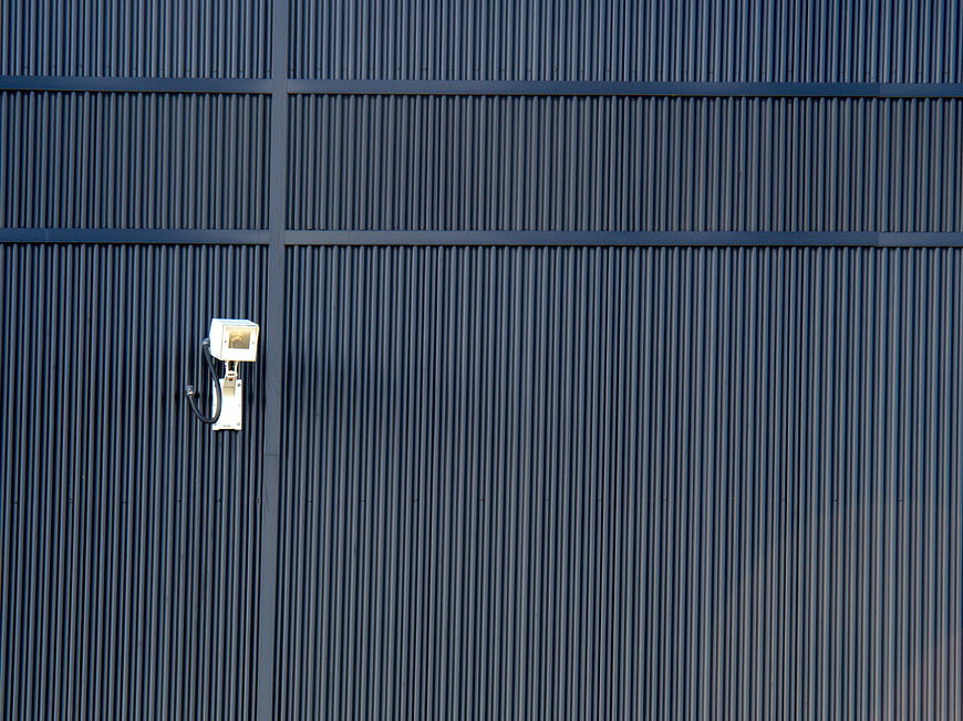 White Security Camera on Blue Corrugated Metal Wall