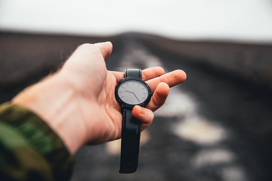 Hand holding minimalist black watch on blurred road background