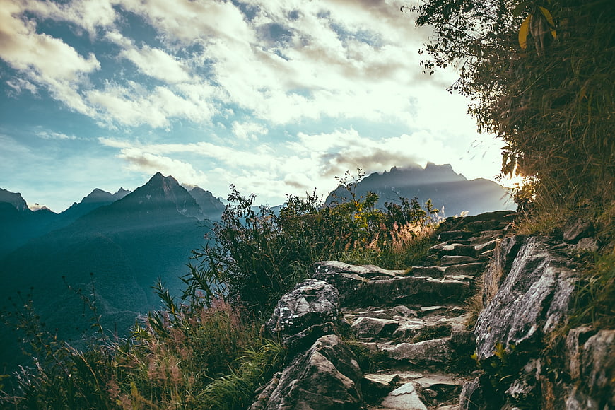 Rugged Mountain Trail with Sun Rays and Cloudy Sky
