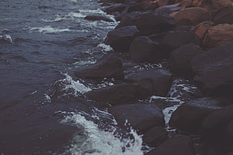Dark moody ocean waves crashing against rocky shore