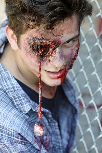 Scary Zombie Man with Bloody Eye Makeup and Chain Link Fence