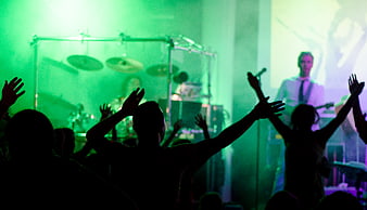 Silhouetted crowd cheering at a live concert with green stage lighting