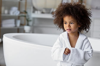 Cute child with curly hair in white bathrobe in bathroom