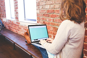 Woman working on laptop in loft with brick wall
