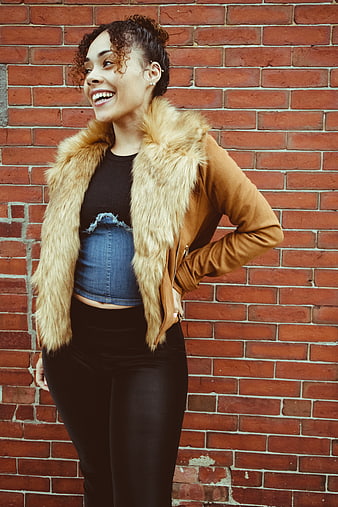 Stylish woman laughing against red brick wall