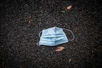 Discarded blue surgical face mask on dark asphalt ground