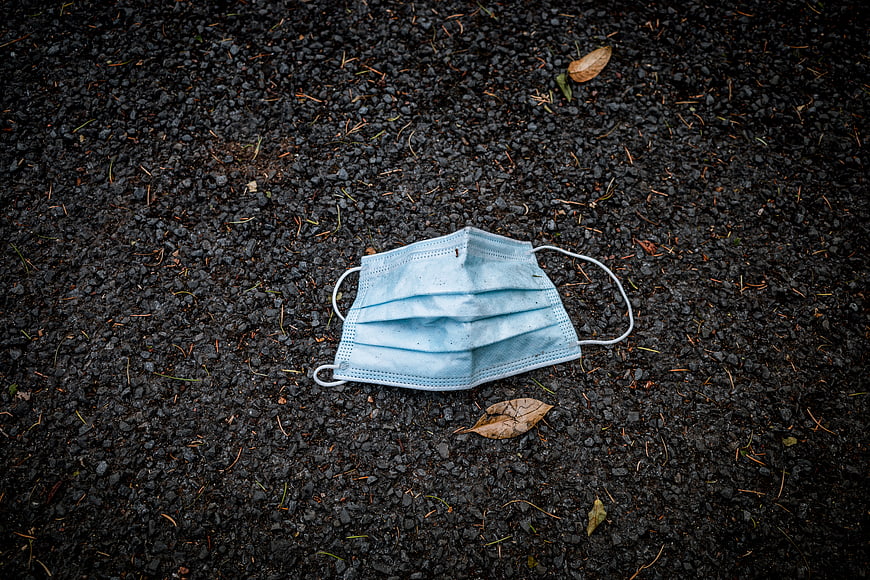 Discarded blue surgical face mask on dark asphalt ground