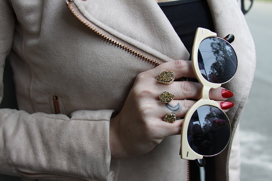 Woman's Hand Holding Sunglasses with Gold Rings and Red Nails