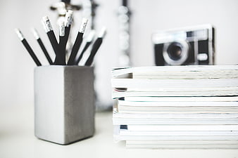 Stack of magazines and pencils in a gray cup on a desk