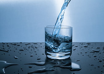 Water Pouring into Glass with Splashes on Dark Surface