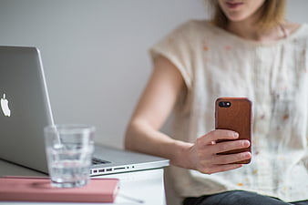 Woman using smartphone at desk with laptop and water glass