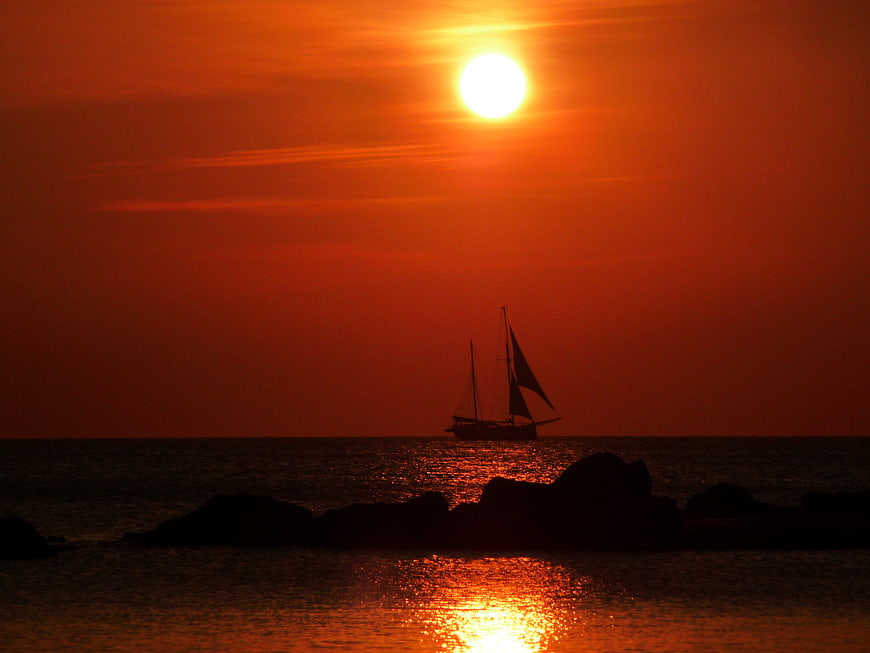 Silhouette of Sailboat on Ocean at Vibrant Red Sunset