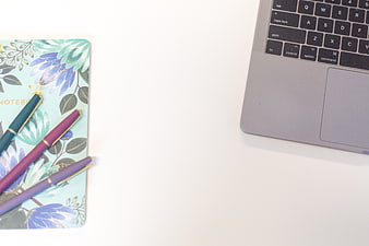 Minimalist workspace with floral notebook, pens, and laptop