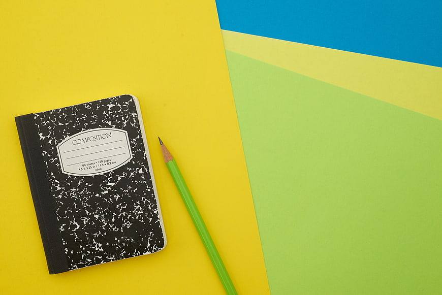 Composition notebook and green pencil on colorful background