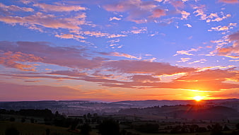 Vibrant Sunset Over Rolling Hills and Misty Valley