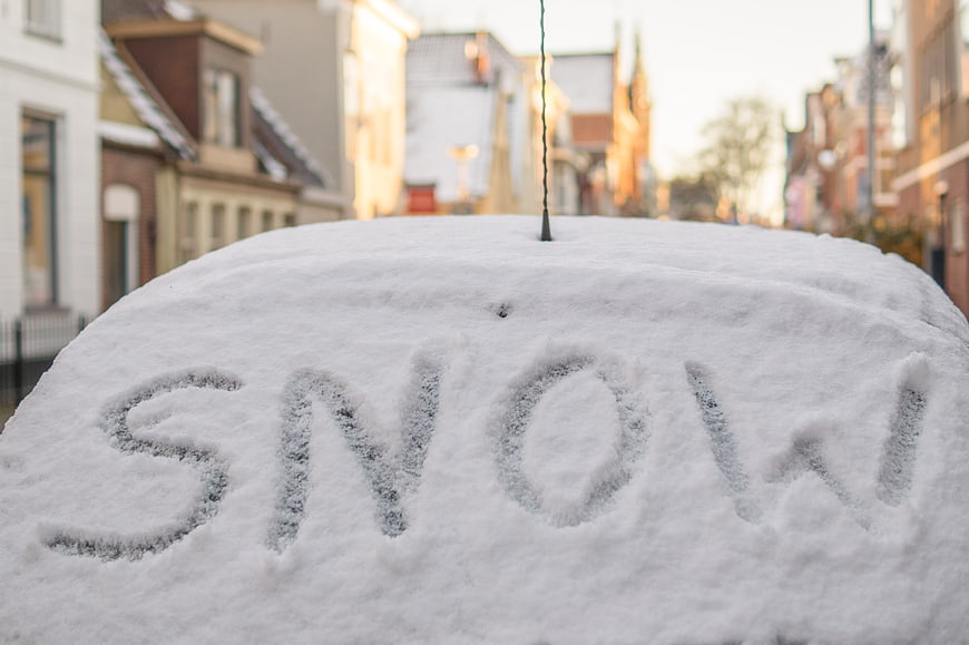 Word Snow Written on Snow-Covered Car Roof in City