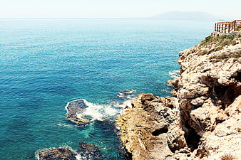 Sunny coastal cliff with turquoise sea and wooden railing