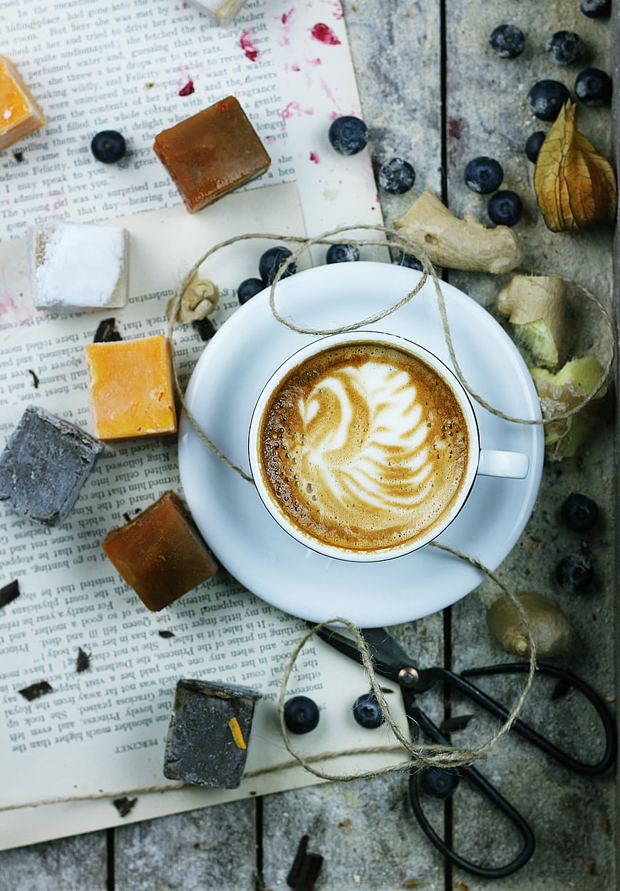 Overhead view of latte art coffee with ginger candies and blueberries