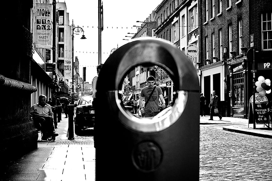 Black and white street photography of a man framed by a bollard