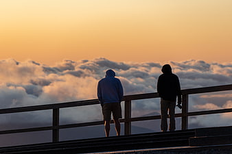 Two people watching sunset over sea of clouds from mountain viewpoint