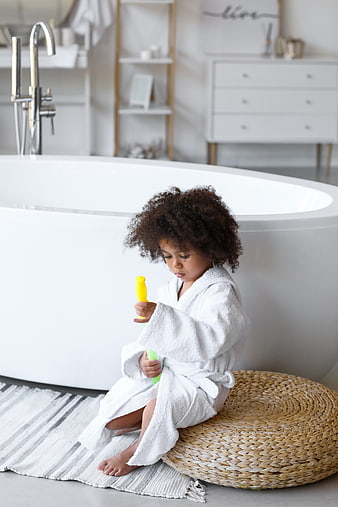Cute child in white robe playing with toys in modern bathroom