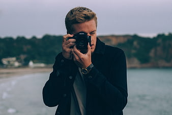 Young male photographer taking photo with Sony camera on beach