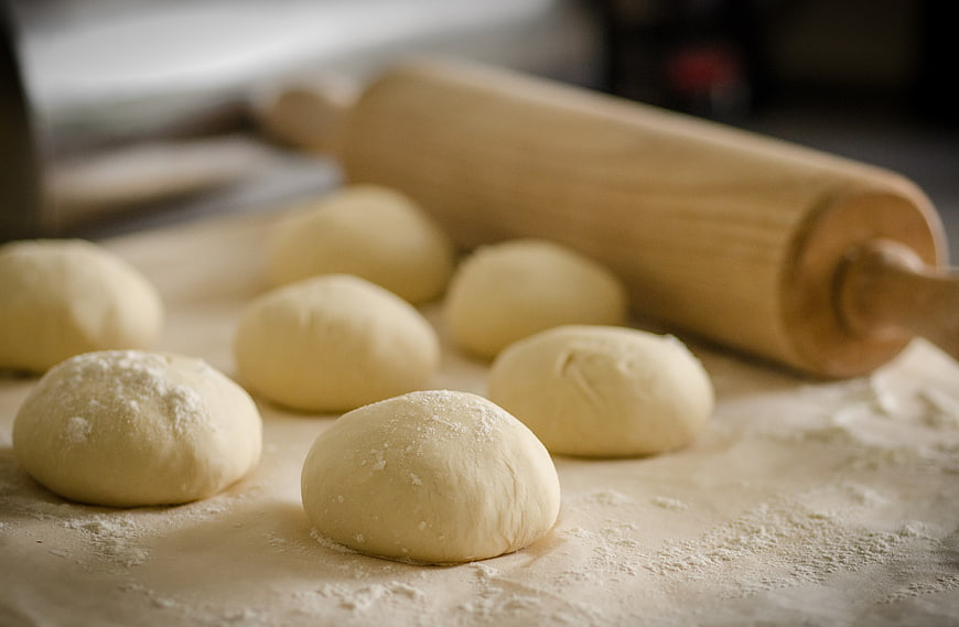 Fresh dough balls and wooden rolling pin on floured surface