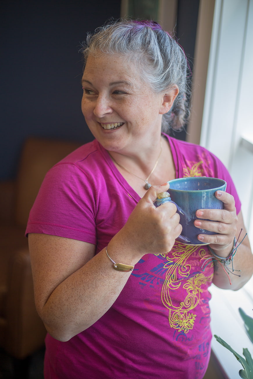 Happy mature woman with purple hair drinking from blue mug