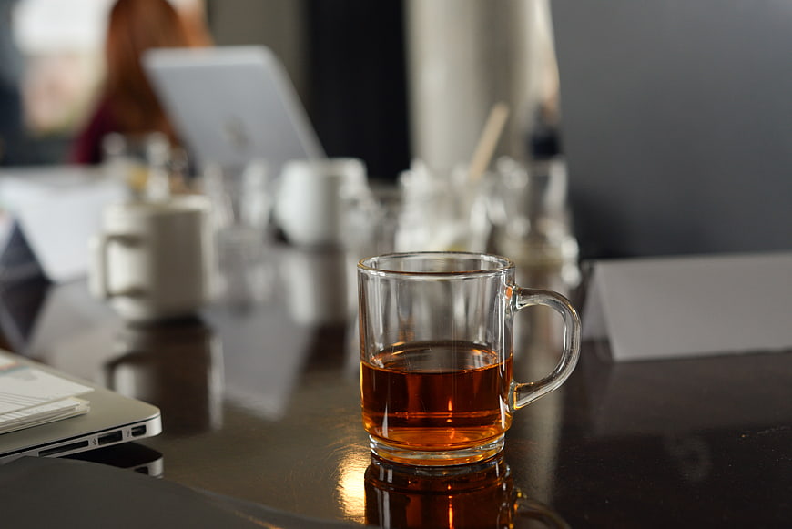 Glass cup of tea on office desk with blurred background