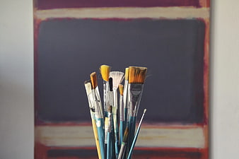 Collection of used paintbrushes in front of abstract painting