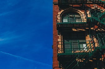 Red Brick Building with Green Fire Escape Against Blue Sky