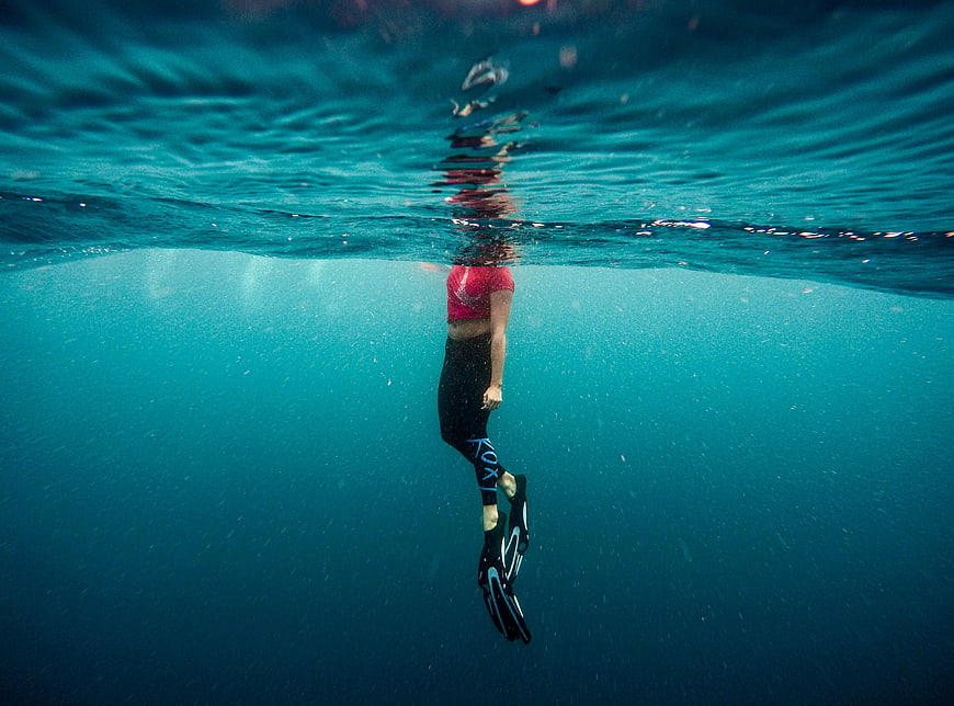 Underwater shot of woman swimming with fins in blue ocean