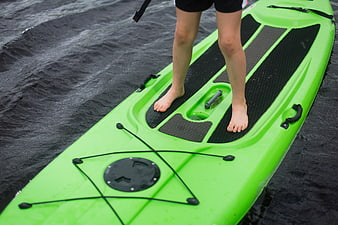 Close-up of bare feet standing on a green kayak in water