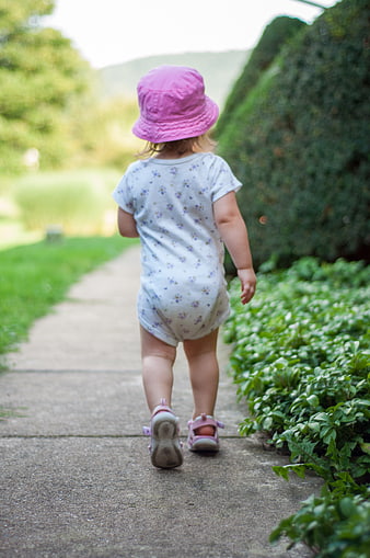 Toddler girl walking away on garden path in pink hat