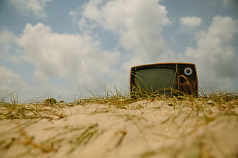 Vintage Television Set in Sandy Grass Under Blue Sky