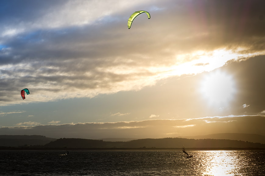 Kite surfers gliding on water during a dramatic sunset