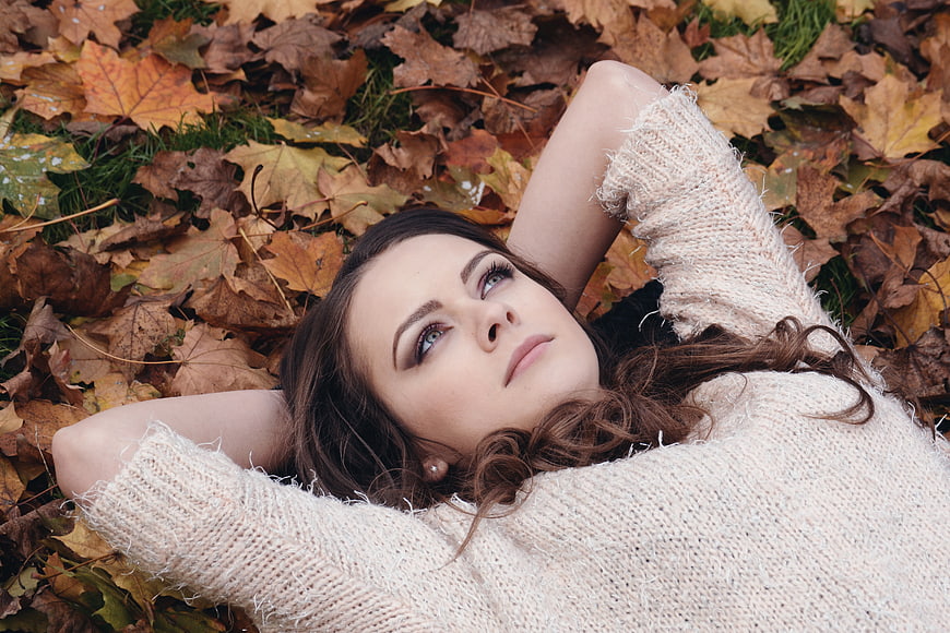 Woman in beige sweater lying on autumn leaves