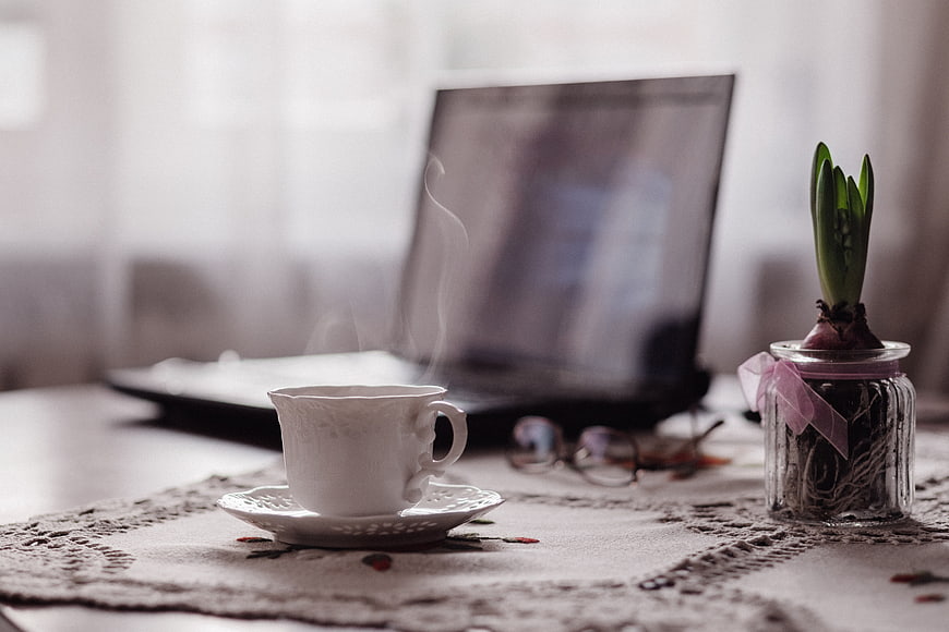 Steaming Tea Cup on Lace Tablecloth with Laptop and Plant