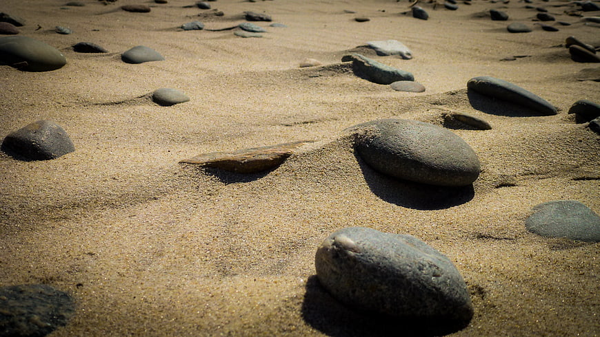 Smooth stones on sandy beach with natural sunlight