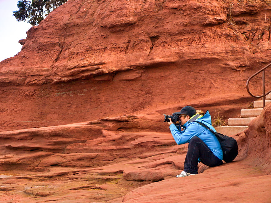 Woman photographer crouching to take photo at red rock cliff