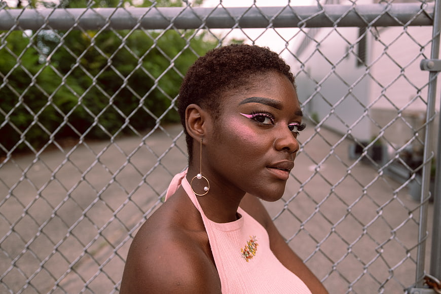 Portrait of stylish Black woman with pink makeup against fence