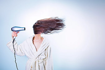 Woman in white bathrobe drying hair with silver hairdryer