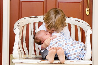Toddler kissing newborn baby on rustic white bench