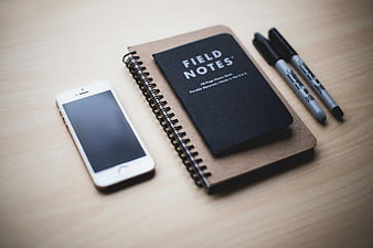 Minimalist workspace with smartphone, notebook, and pens on wooden desk
