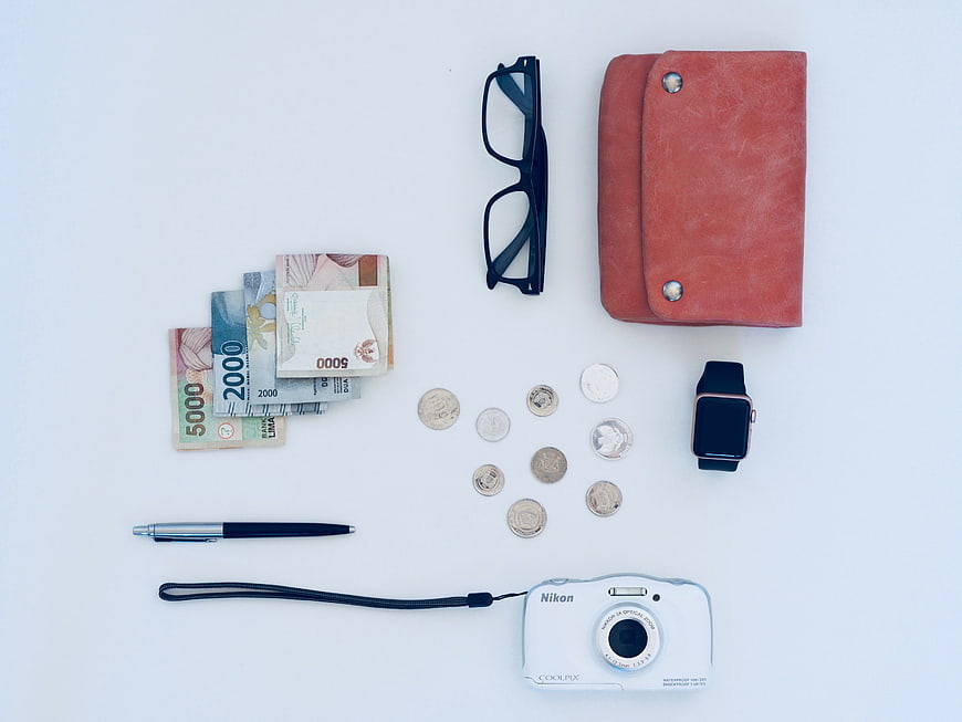 Flat lay of travel essentials, cash, camera, and accessories on white