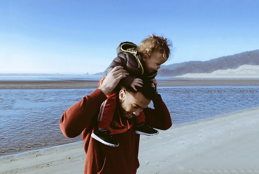 Father carrying toddler on shoulders at sandy beach