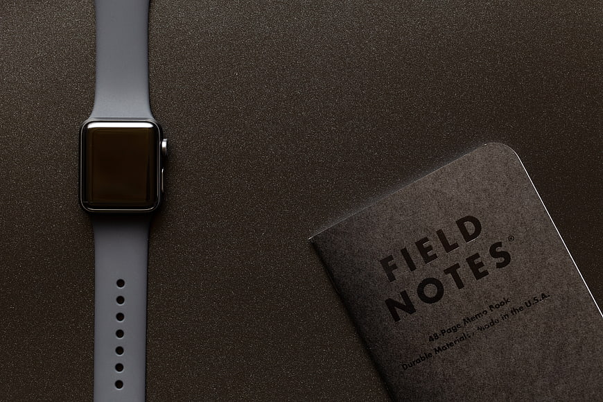 Smartwatch and Field Notes Notebook on Dark Textured Surface