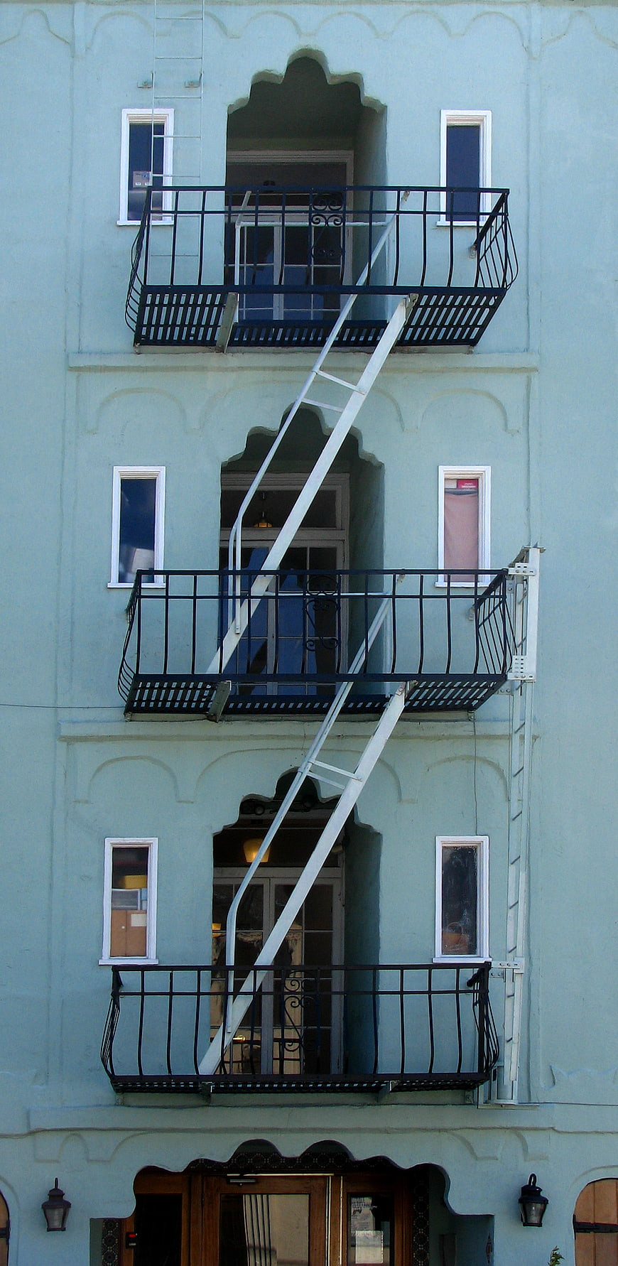 Vertical view of light blue building facade with fire escape